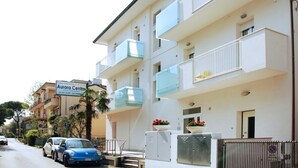 Un hotel de varios pisos con balcones, un cartel y una zona de estacionamiento.