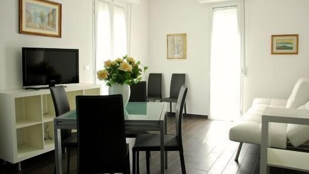 Una sala de estar moderna con un televisor de pantalla plana, una mesa de comedor con sillas, un sofá blanco y un jarrón con flores.