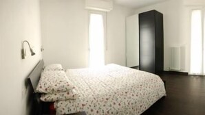 Un dormitorio con una cama, una mesita de noche, una lámpara de pared y un ventanal grande.