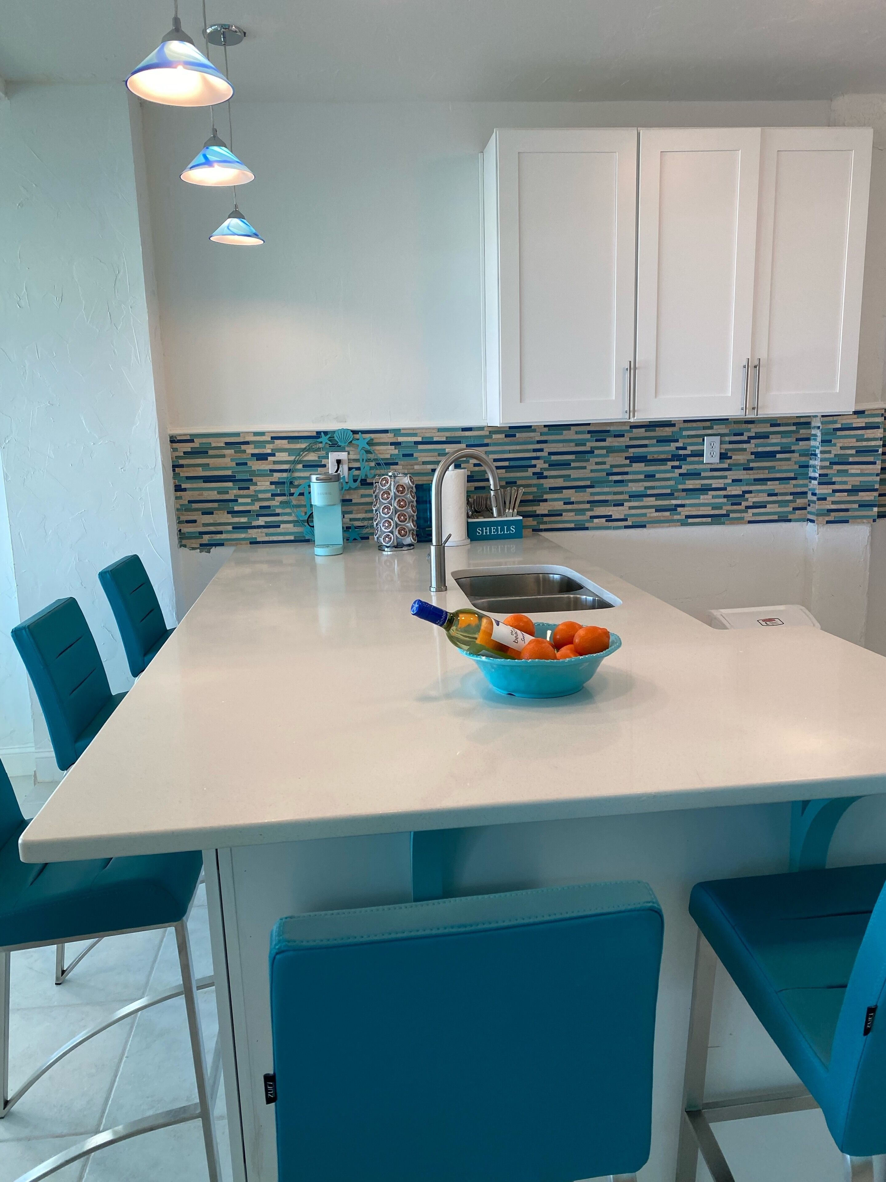 Una cocina con encimera blanca, sillas azules, un fregadero y un salpicadero con azulejos azules y blancos.