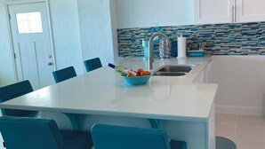 Una cocina moderna con una isla central, sillas azules y lámparas colgantes.