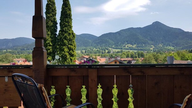 A wooden balcony with a view of a town and mountains.