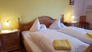 A double bed with white linens and pillows, a bedside table with a lamp, and a chair with a red cushion.
