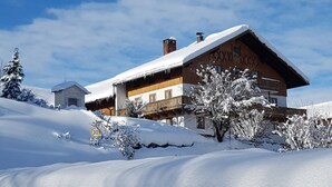 A wooden chalet with a snow-covered roof, surrounded by snow-covered trees and a clear sky.