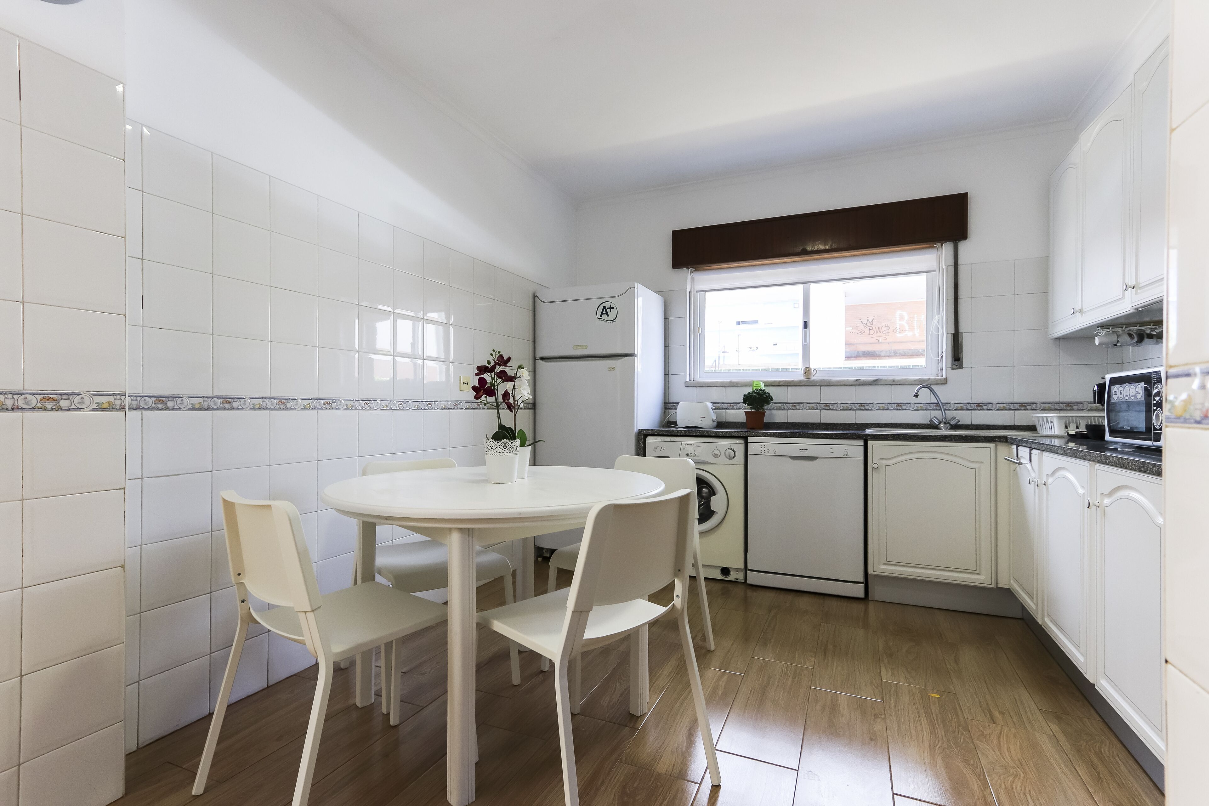 Een keuken met witte kasten, een witte koelkast, een wasmachine en een eettafel met stoelen.