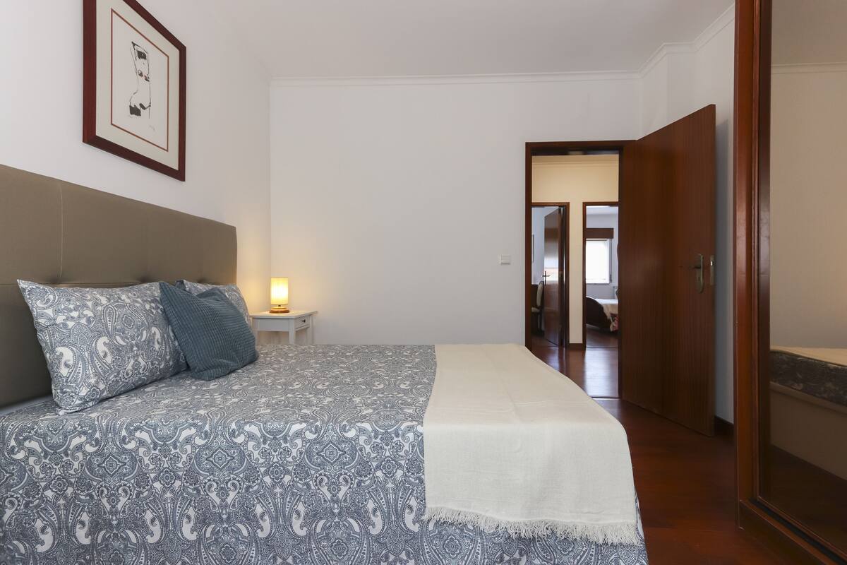 A bedroom with a patterned bedspread, a bedside lamp, and a framed picture on the wall.