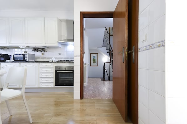 Une cuisine avec des meubles blancs, un four à micro-ondes, un four traditionnel et un coin repas avec une chaise blanche.