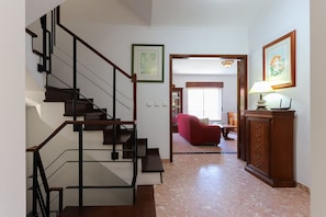 A staircase with a wooden handrail and black railings, leading to a living area with a red sofa and a wooden cabinet.