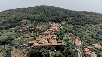 A village with terracotta-roofed buildings, narrow winding roads, and lush green hills in the background.