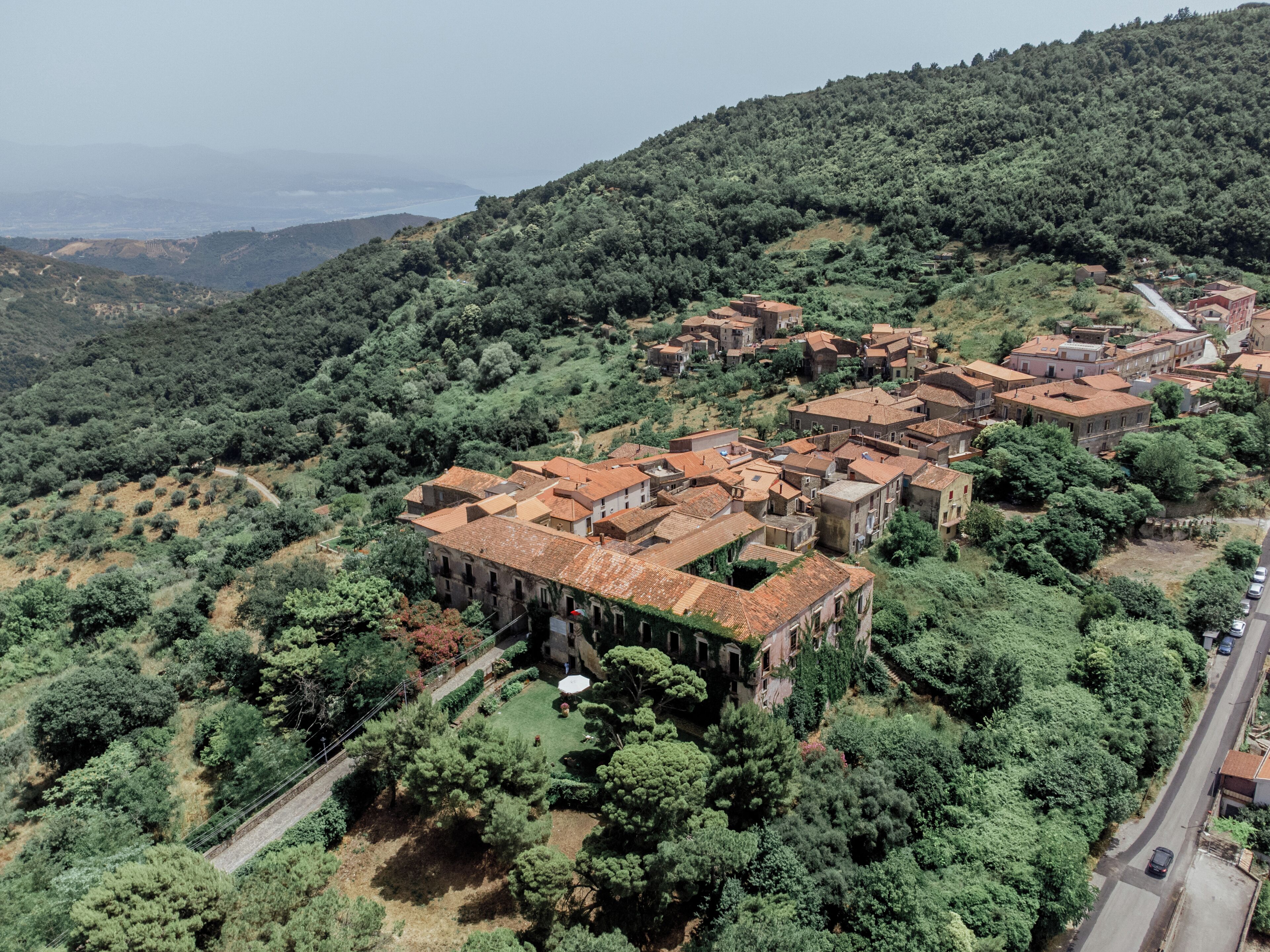 Vista aérea de un pueblo en una ladera con edificios tradicionales, calles estrechas y abundante vegetación.