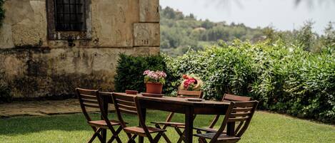 A wooden table and chairs set outdoors with a stone wall and greenery in the background.