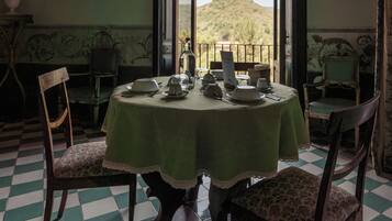 Comedor con una mesa preparada para cuatro personas, sillas, vista a una colina y piso de tablones de ajedrez.