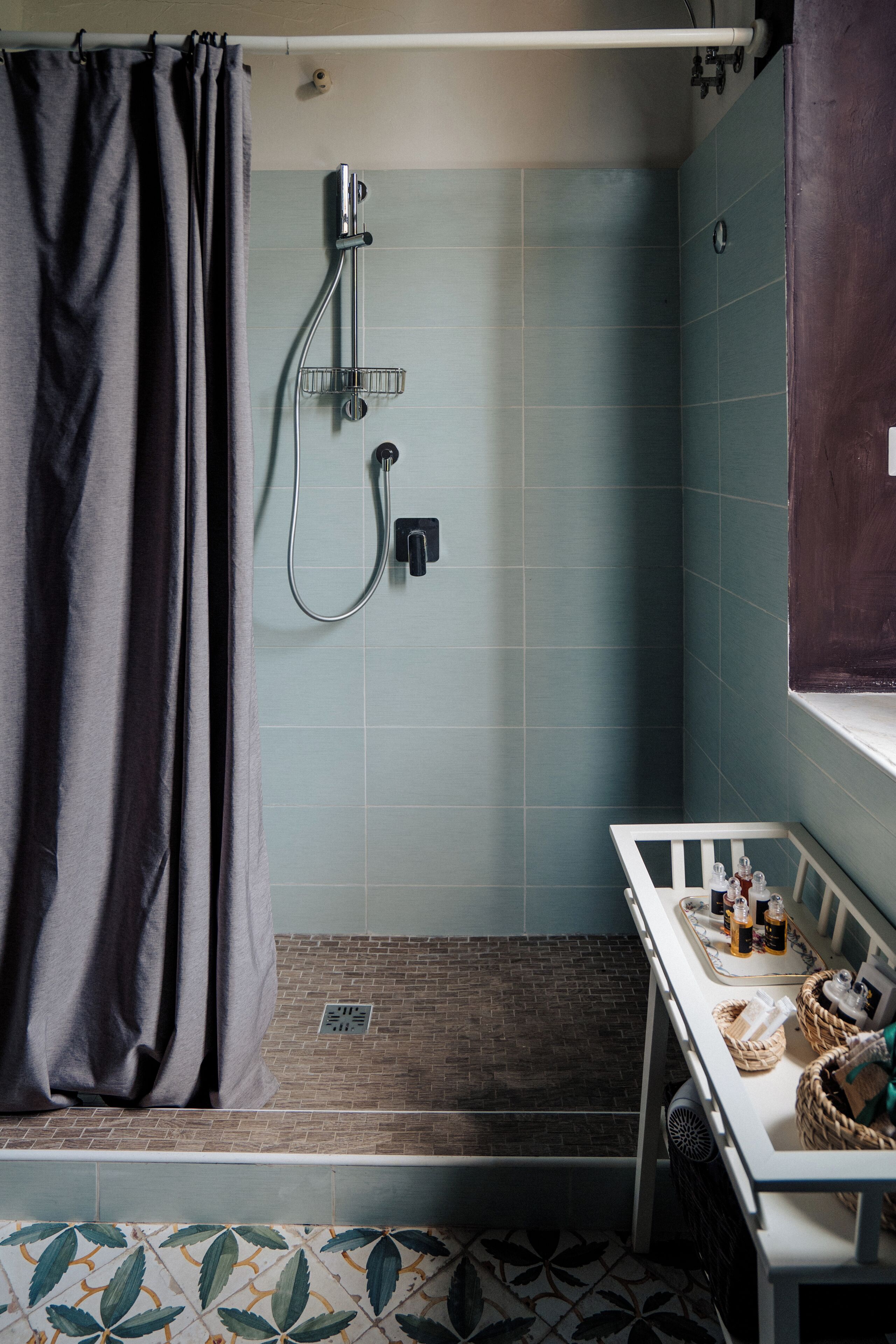 A bathroom with a shower, a sink with toiletries, and a patterned floor.