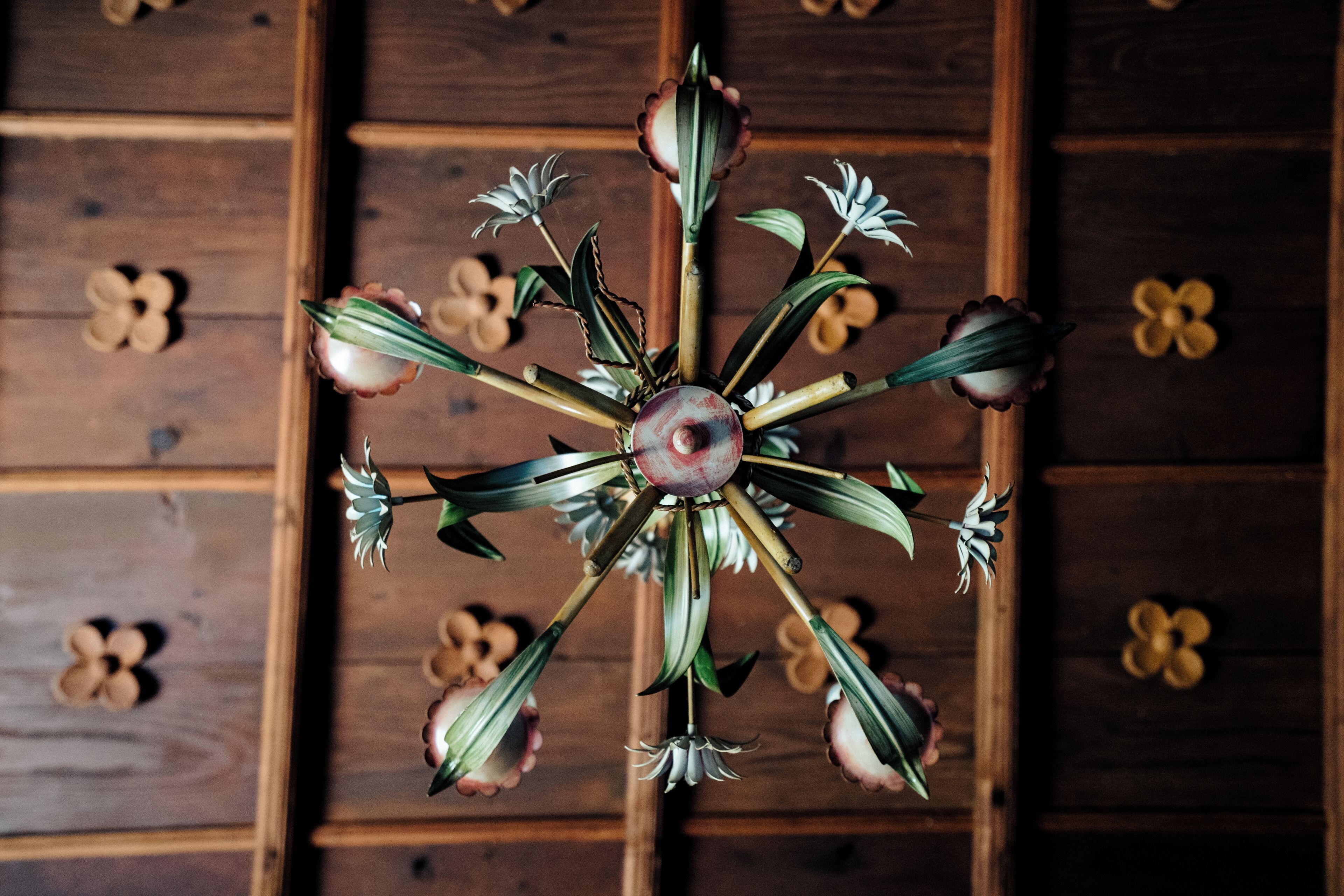 A chandelier with multiple arms and flowers, hanging in front of wooden paneling with floral designs.
