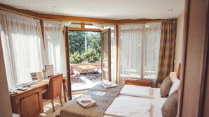 Een hotelkamer met een bed, bureau en stoel, een groot raam met gordijnen, en uitzicht op de omgeving.