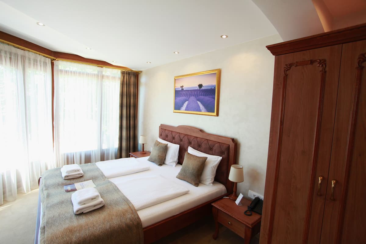 A hotel room with a large bed, two bedside tables, a wardrobe, and a painting on the wall.