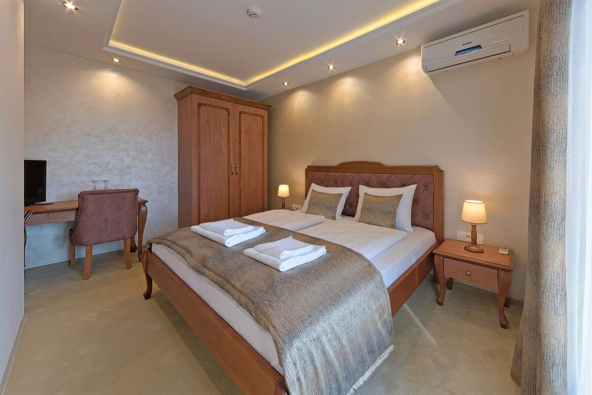 A neatly arranged bedroom with a bed, bedside table, lamp, and a desk with a chair.