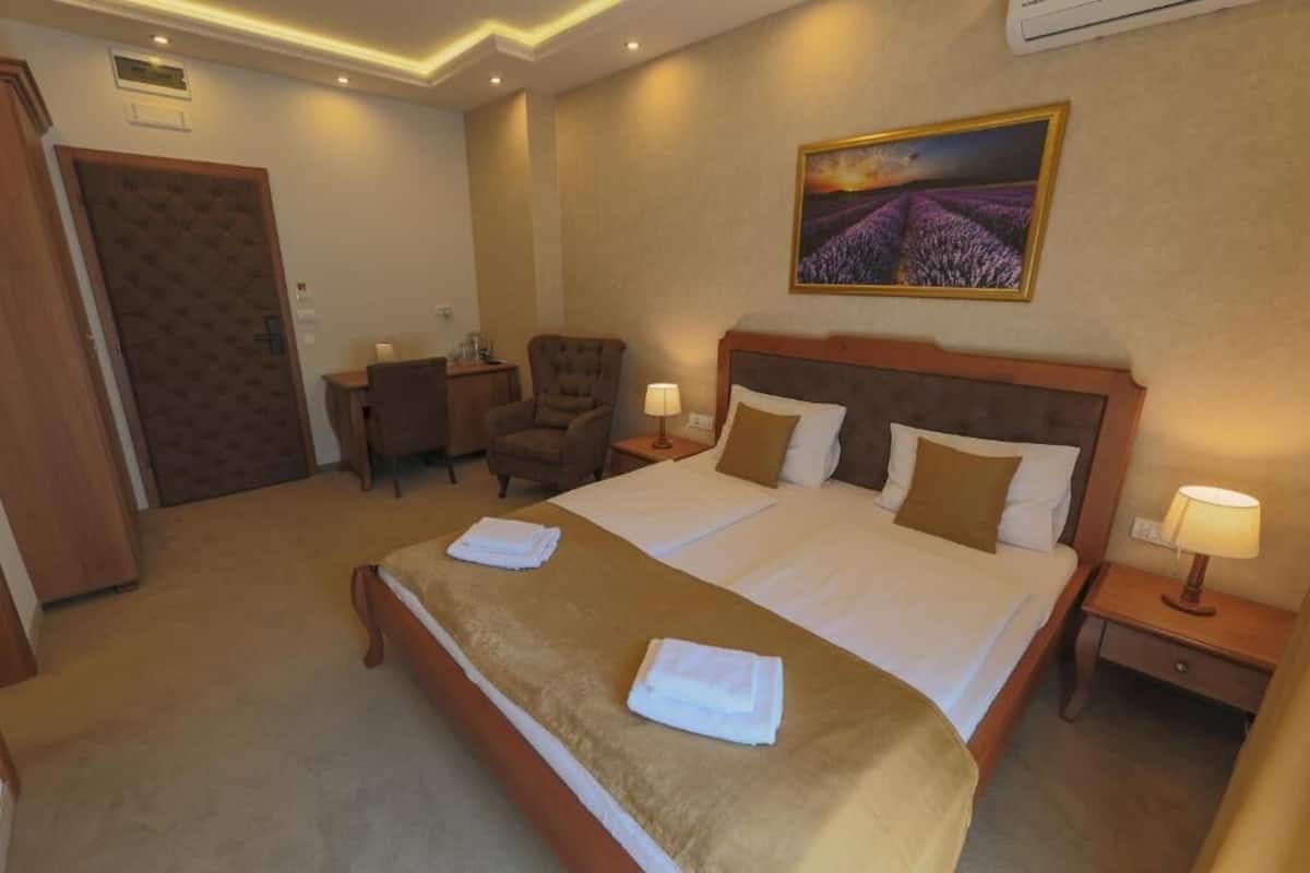 A hotel room with a large bed, two bedside tables, a chair, and a painting on the wall.