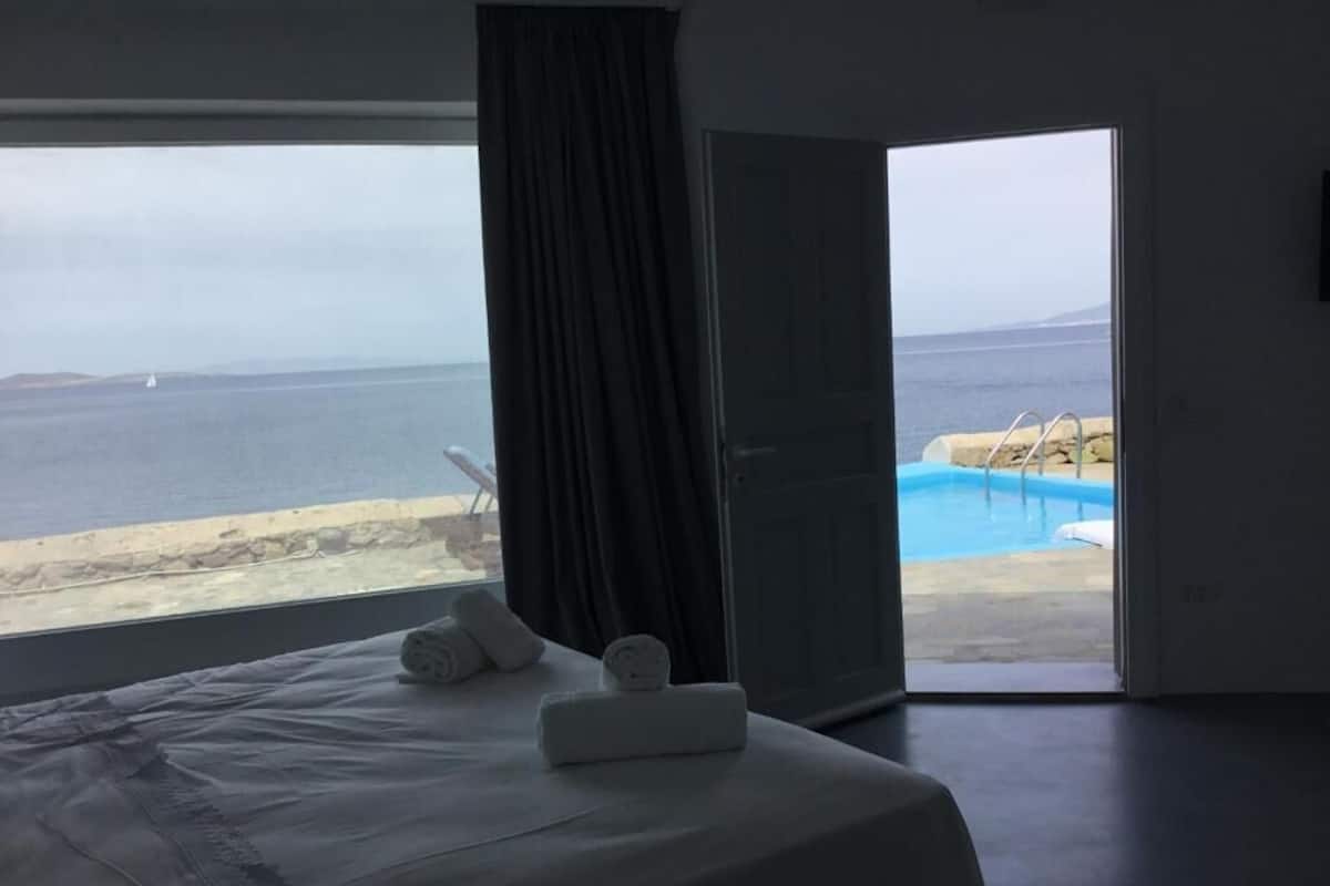 A bedroom with a bed, a window, and a view of the sea and a swimming pool.