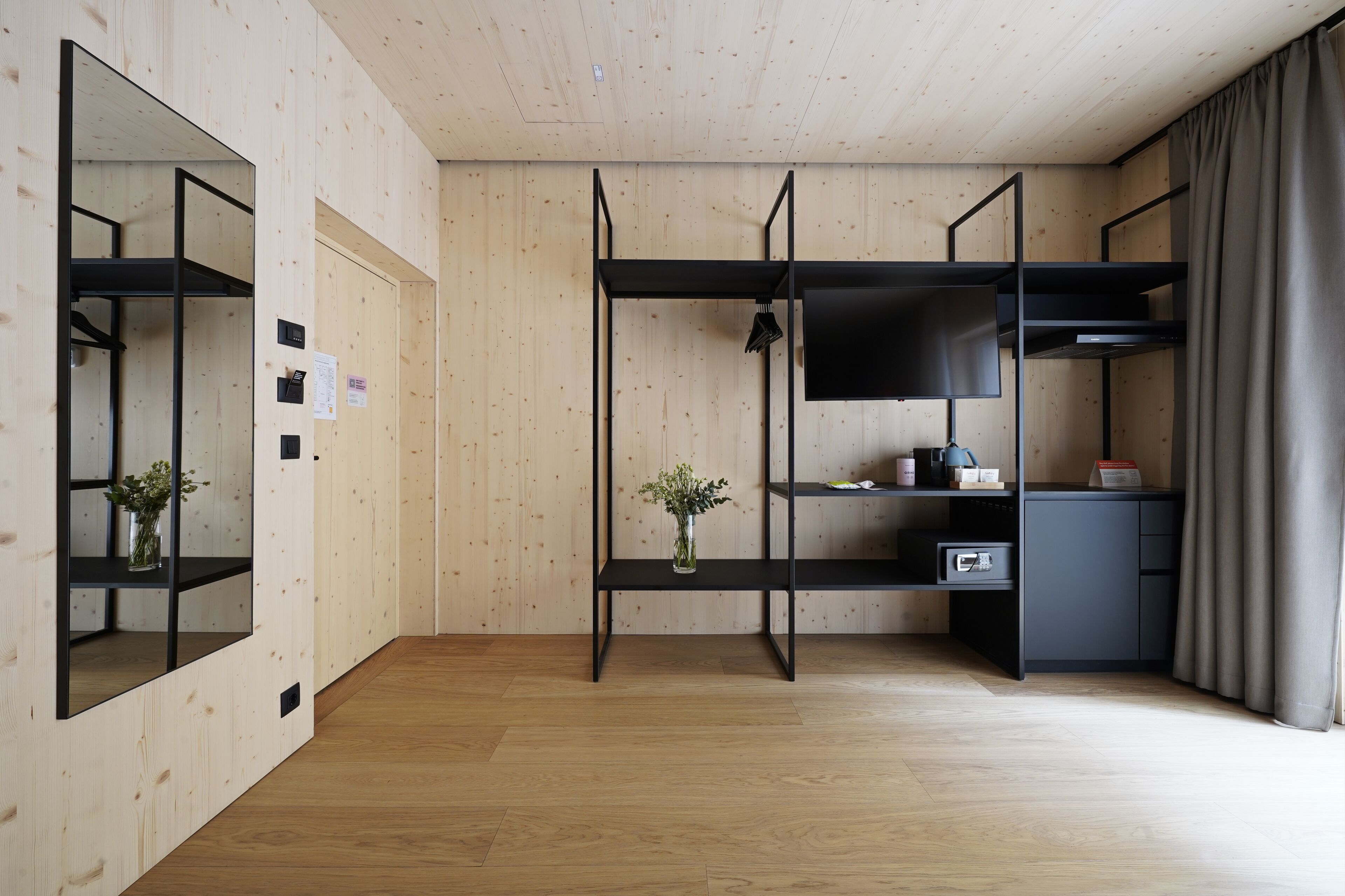 A modern room with wooden walls, a wooden floor, a black TV on a shelf, a small plant, and a desk with a computer.
