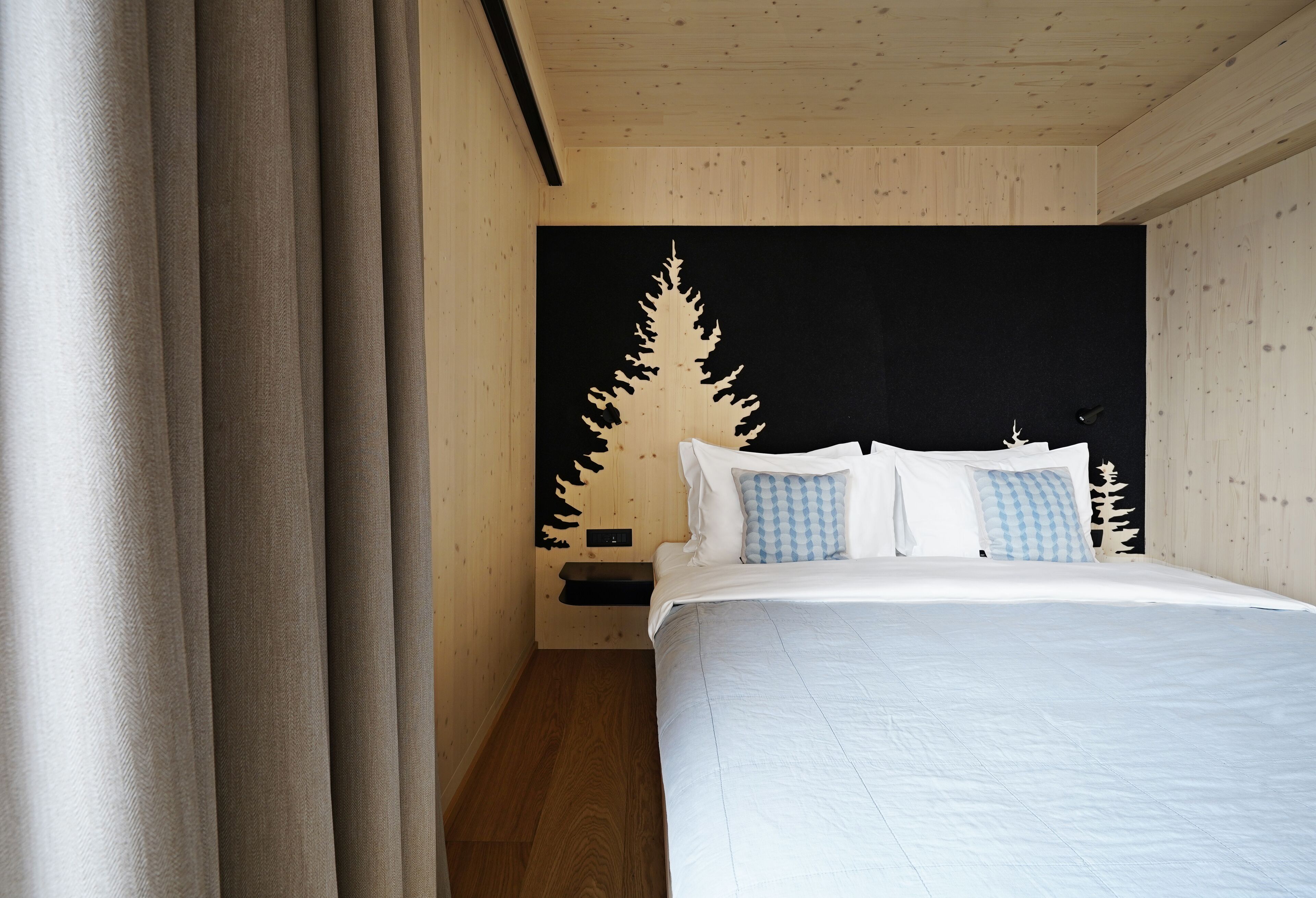 A bedroom with a bed, curtains, a nightstand, and a wall-mounted shelf.