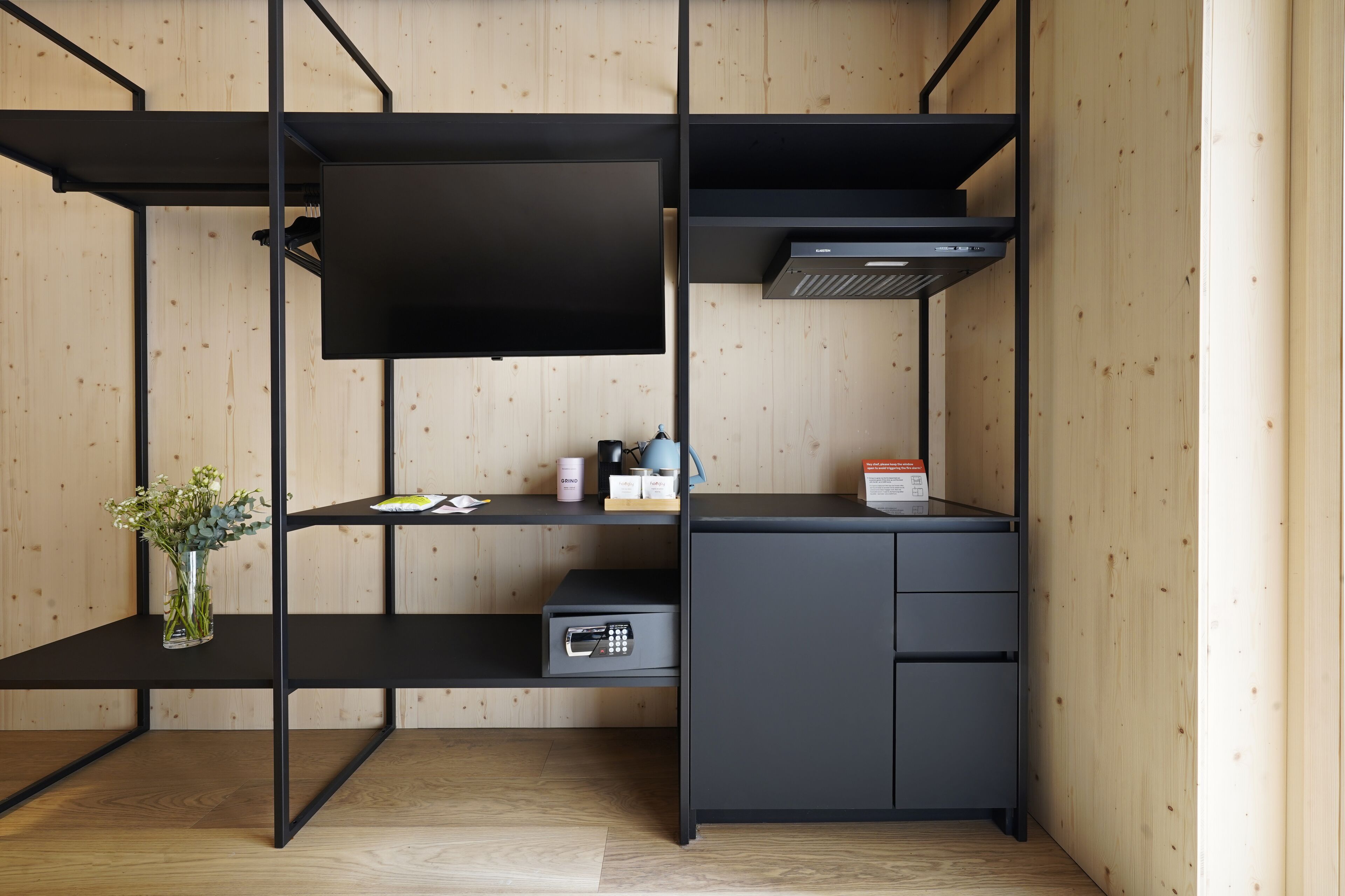 Ein modernes, kompaktes Zimmer mit schwarzem Schreibtisch, einer kleinen Küchenzeile und einer integrierten Heizung.