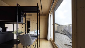 Ein modernes Zimmer mit Holzboden, Schreibtisch und Stuhl, großem Fenster und Balkon mit Geländer.