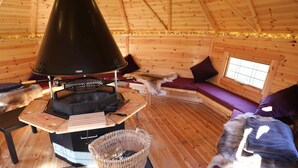 L’intérieur chaleureux d’un chalet avec un poêle à bois, un panier en osier et une fenêtre avec des rideaux.