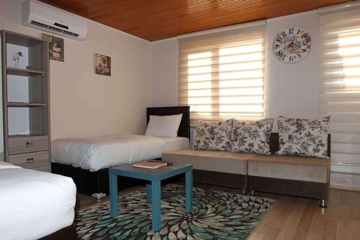 A bedroom with a bed, a sofa, a small table, and a wall clock.