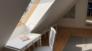 A room with a sloped ceiling, a white desk with a lamp, a chair, and a small table with decorative items. - 80 m from the beach, everything in view - Anchorage vacation apartment (Rostock-Warnemünde)