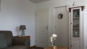 A living room with a sofa, a small table with a vase of flowers, a cabinet with glassware, and a door. - 80 m from the beach, everything in view - Anchorage vacation apartment (Rostock-Warnemünde)