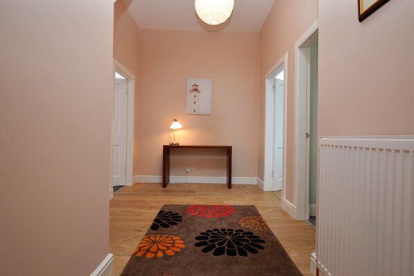 A hallway with a wooden floor, a table with a lamp, and a framed picture on the wall.