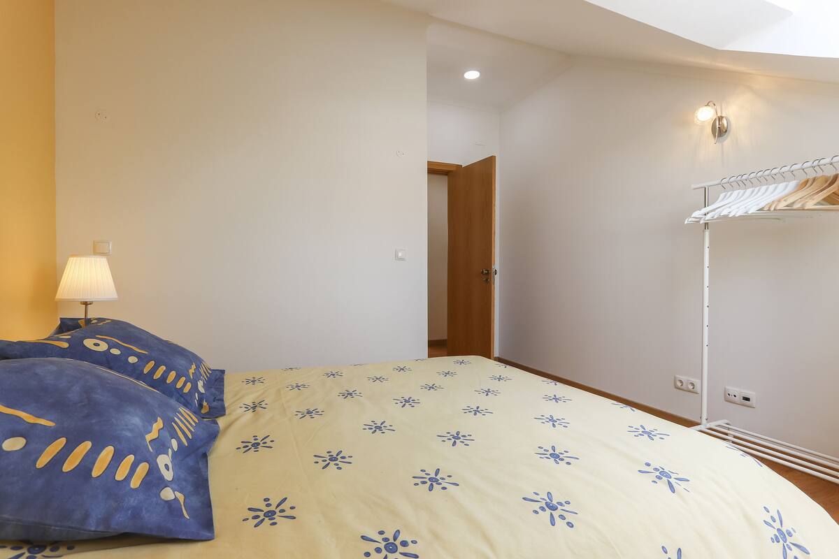 A bedroom with a bed, a bedside lamp, a wardrobe, and a door leading to another room.