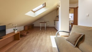 A loft-style living space with a sloped ceiling, a television, a sofa, ottomans, and a small table. - Relaxing Guesthouse - Sónia's Houses (Lisbon)
