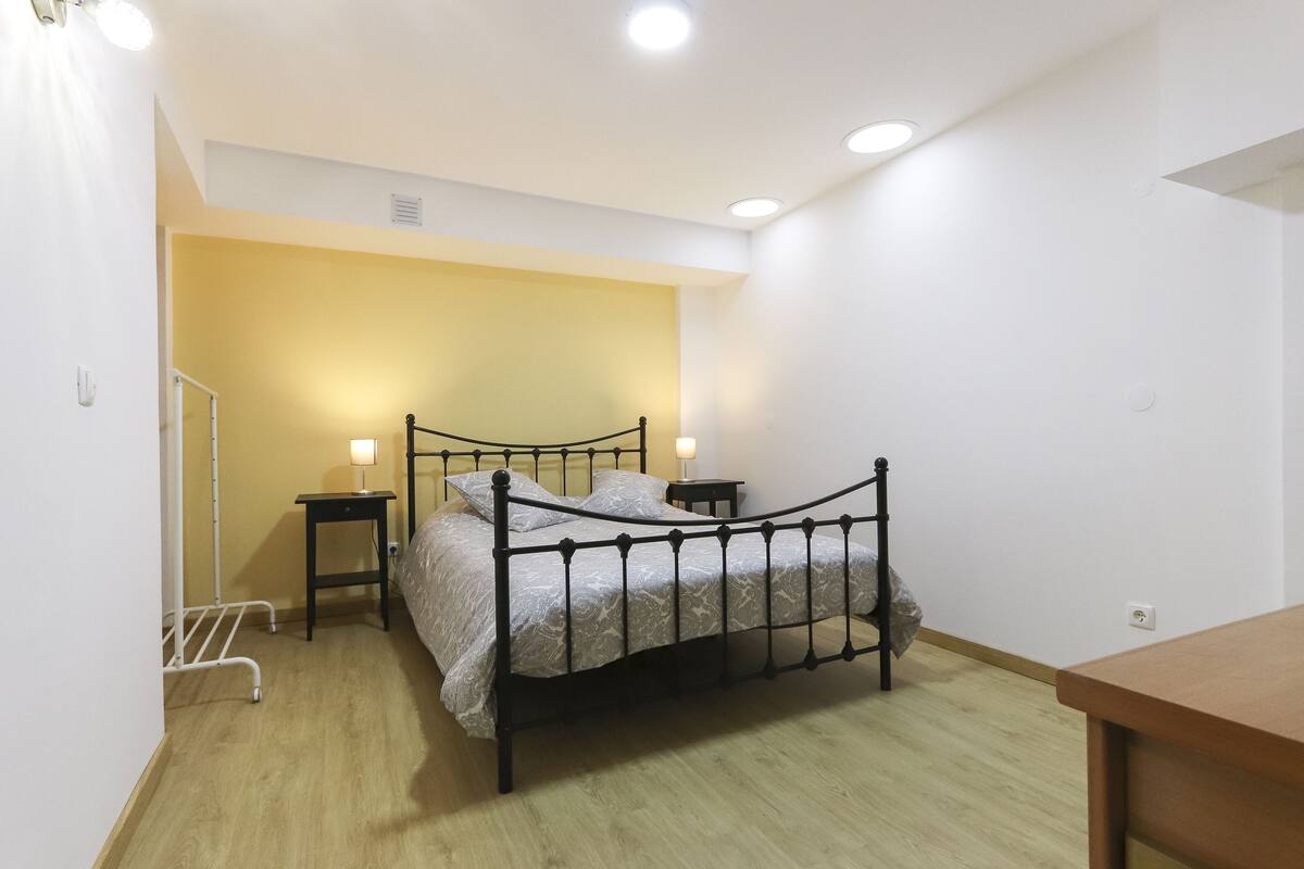 A bedroom with a metal bed frame, a bedside table with a lamp, and a wooden floor.