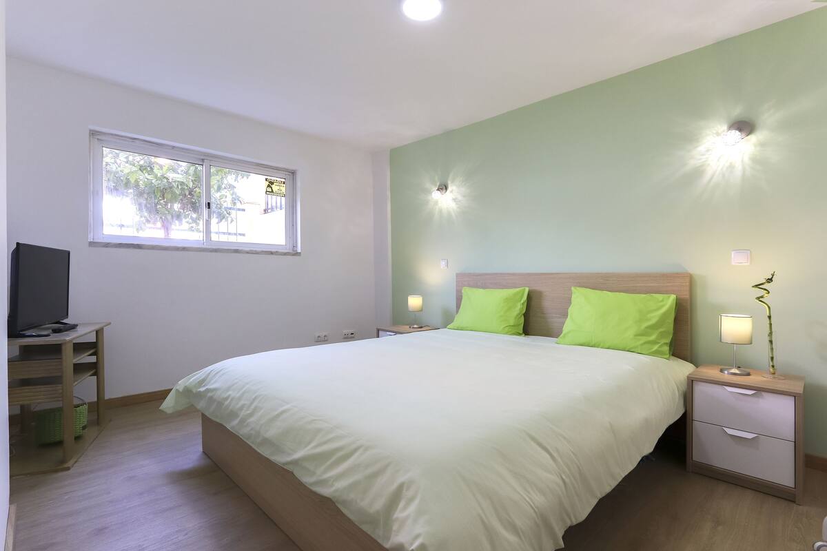 A bedroom with a bed, bedside tables, a TV, and a window.