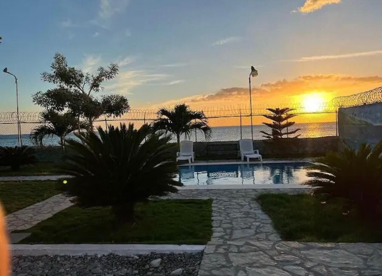 Un espace piscine avec des chaises longues et une vue sur le coucher de soleil sur l’océan.