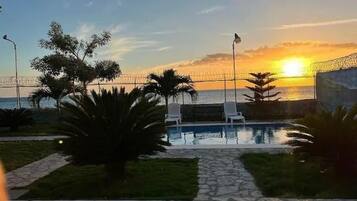 Un espace piscine avec des chaises longues et une vue sur le coucher de soleil sur l’océan.