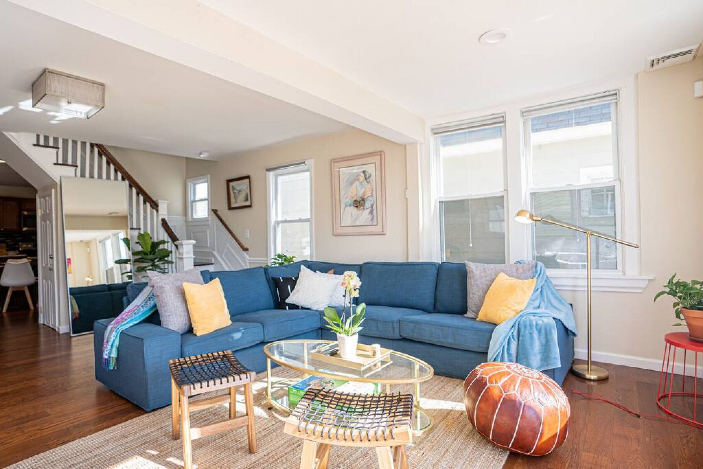 A living room with a blue sectional sofa, a glass coffee table, and a wooden ottoman.