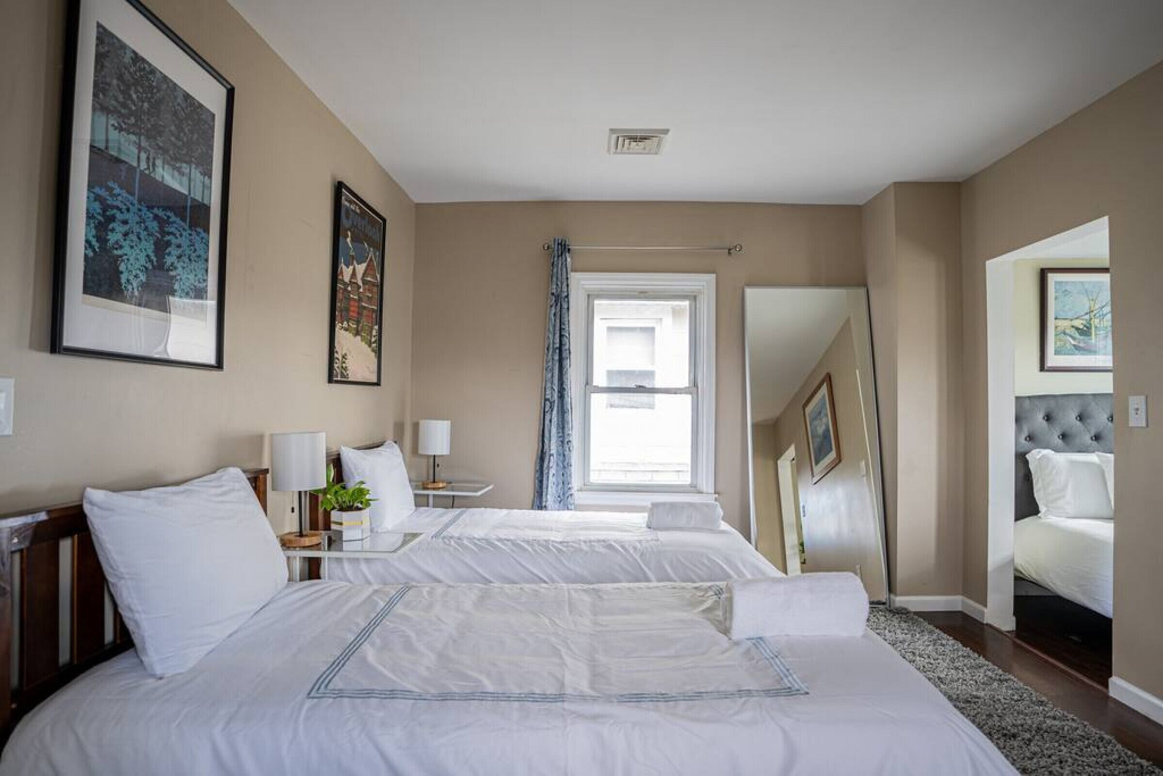 Een hotelkamer met twee bedden, een groot raam met gordijnen, een spiegel en prestaties aan de muur.