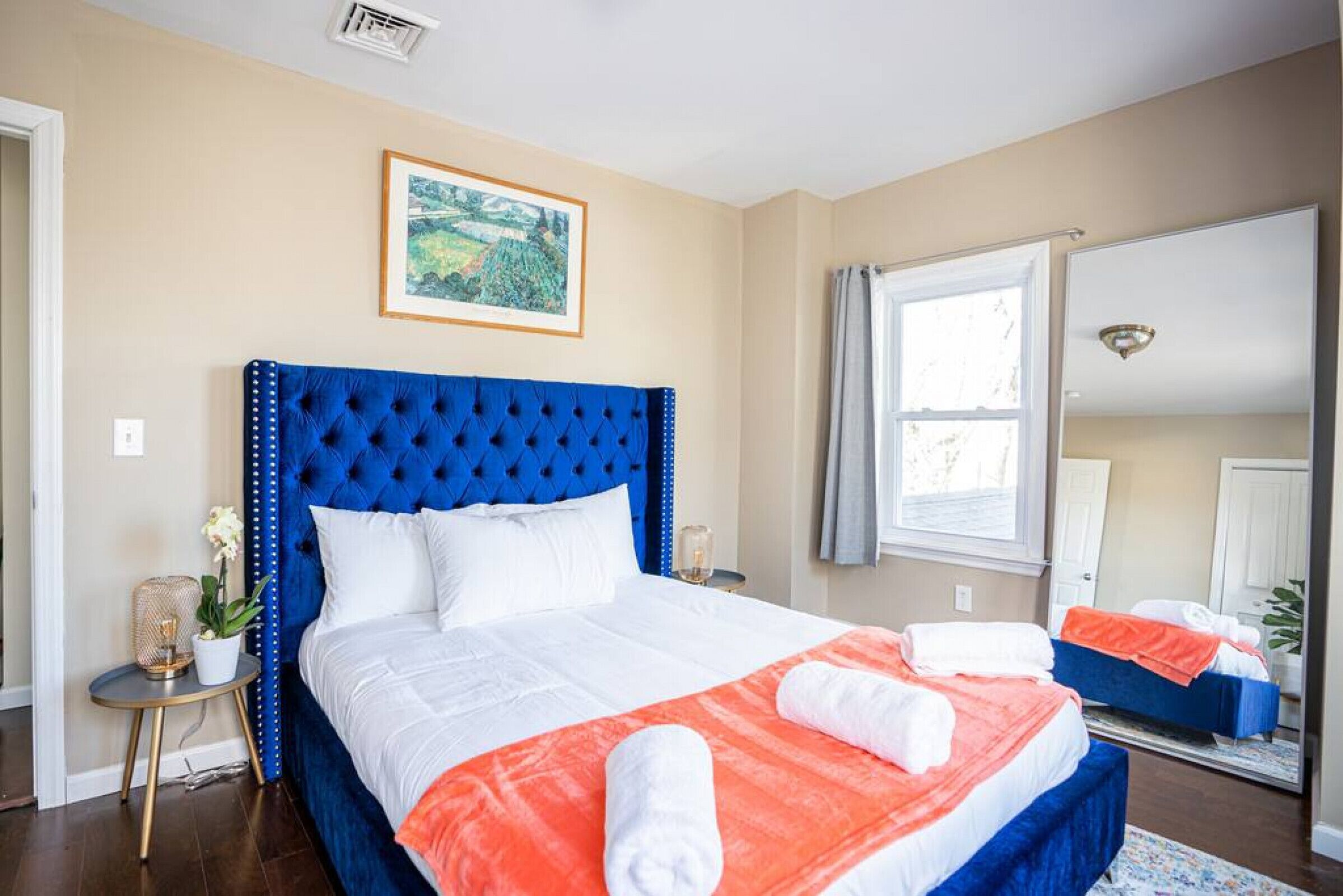 A bedroom with a large bed, a mirror, a window with curtains, and a painting on the wall.