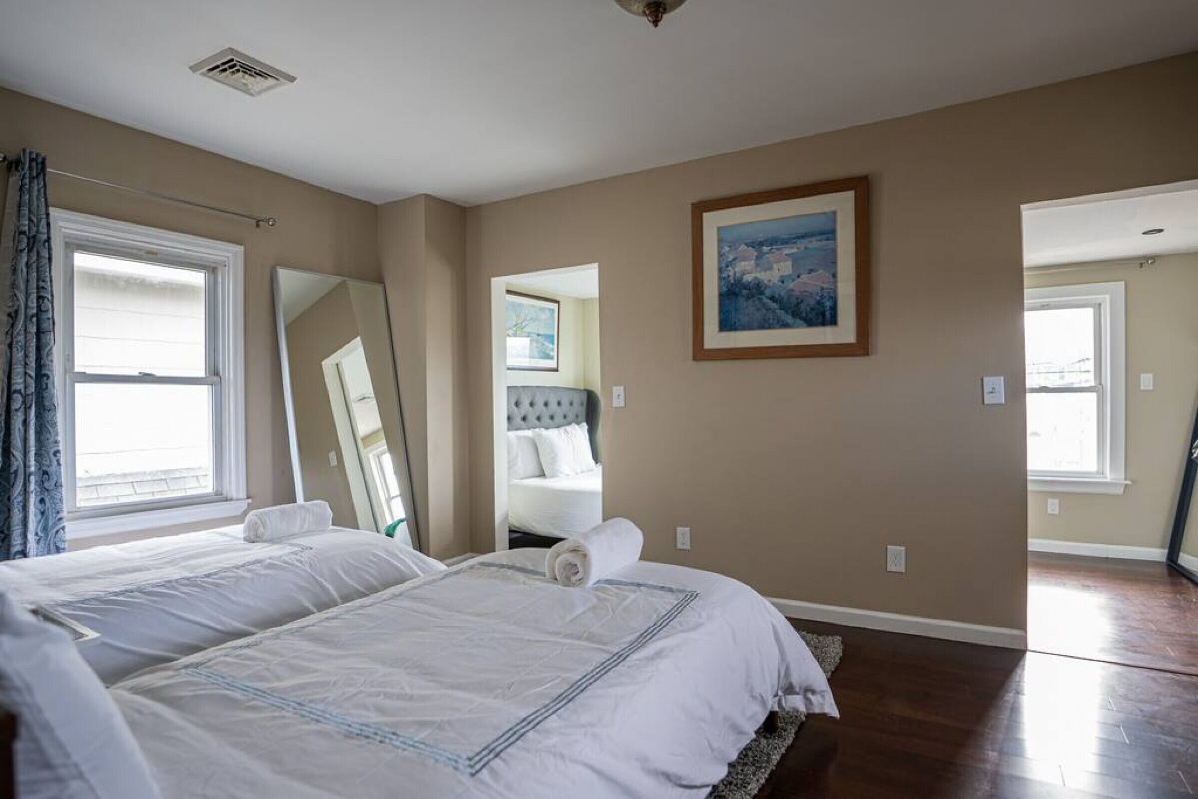 Un dormitorio con una cama grande, un espejo, un cuadro y vistas a otra habitación.