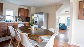 Una cocina moderna con comedor, que incluye un refrigerador de acero inoxidable, armarios de madera y una amplia mesa de comedor con sillas blancas.