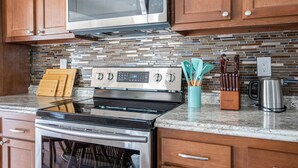 Una cocina con armarios de madera, un microondas de acero inoxidable, una estufa y salpicadero de azulejos.