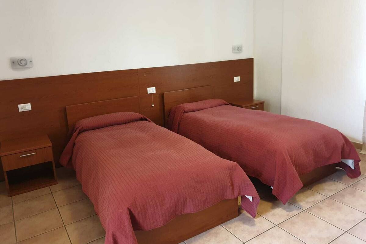 A room with two single beds, wooden headboards, bedside tables, and a tiled floor.