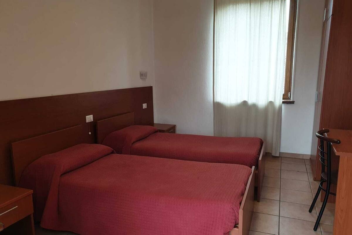 A room with two single beds, a wooden headboard, a small wooden table, and a window with curtains.