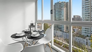 A modern dining area with a glass table, white chairs, and a view of high-rise buildings. - Declan - Designer Gem *Wi-Fi Views Parking (Southbank)