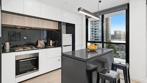 A modern kitchen with a central island, built-in oven, and a large window offering a city view. - Declan - Designer Gem *Wi-Fi Views Parking (Southbank)