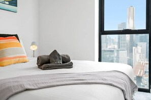 A bed with a white sheet, a rolled-up towel, and a pillow with stripes.