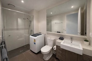 Un bagno moderno con doccia vetrata, un WC bianco, un lavandino con specchio e una piccola pianta in vaso.